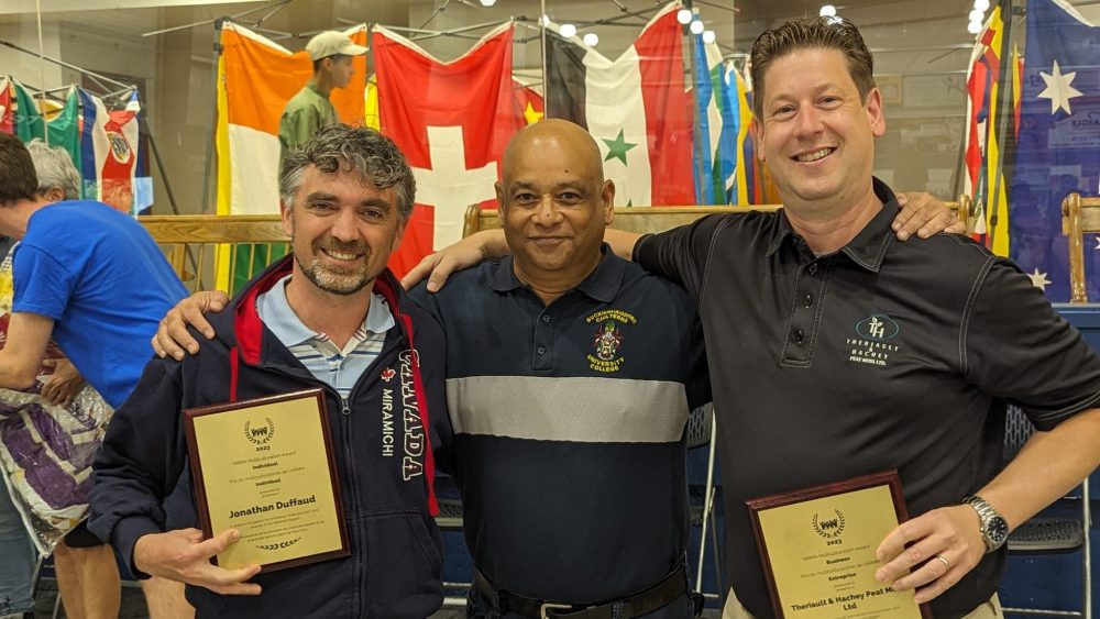 Trois hommes posent pour la caméra, plaques à la main.