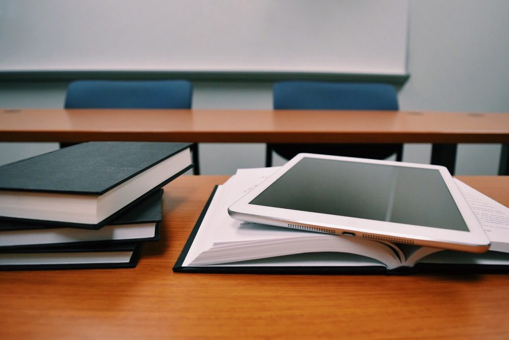 Gros plan sur des livres posés sur une table, avec une tablette numérique posée sur le dessus.