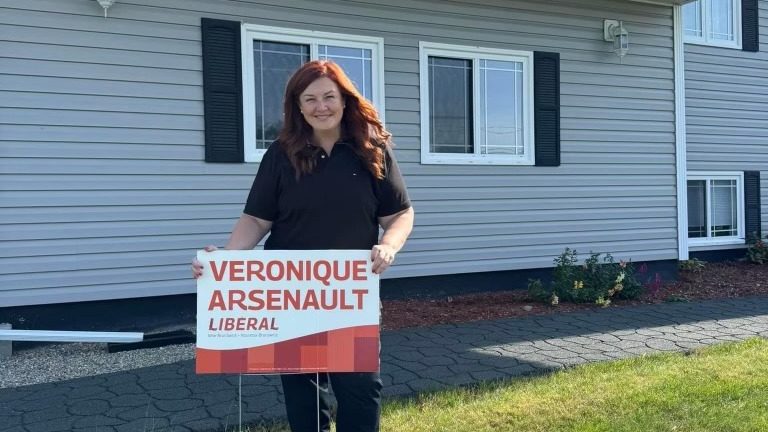 Plan moyen sur Véronique Arsenault, tenant l'une de ses pancartes électorales.