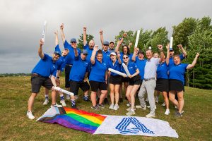 Photo de groupe d'employés de B Corp, placés derrière un drapeau de la fierté et un drapeau arborant le logo de l'entreprise.