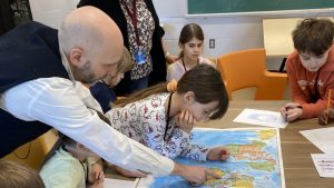 Un adulte entouré d'enfants pointe un pas sur une carte du monde posée sur une table.