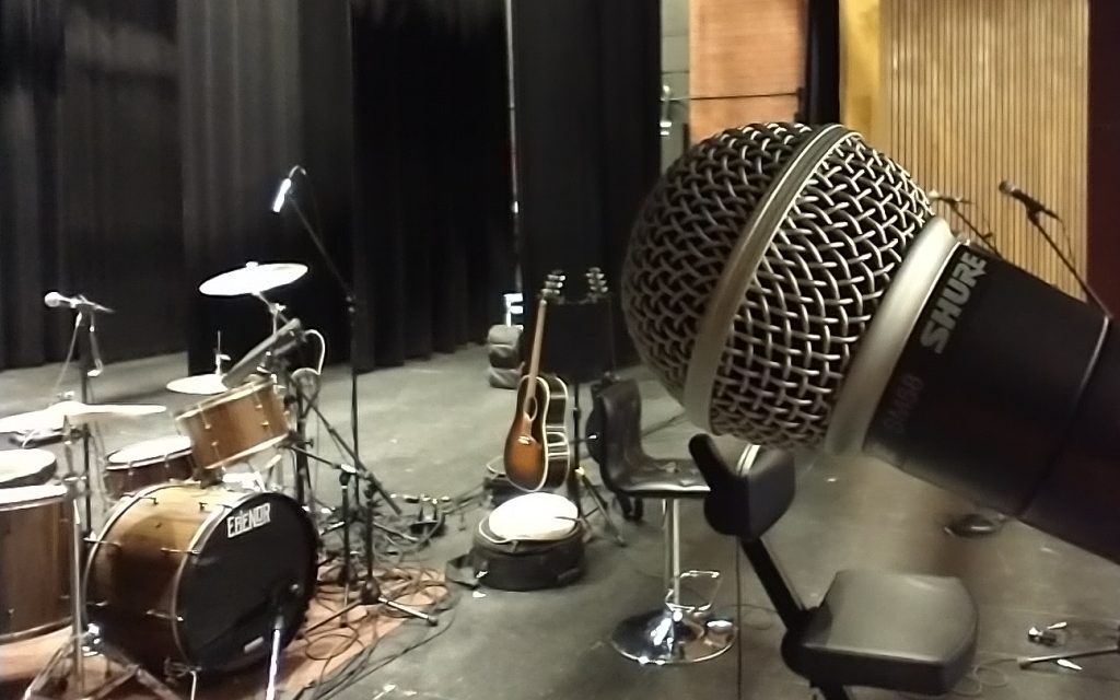 Gros plan d'un microphone sur une scène, avec divers instruments de musique en arrière-plan.