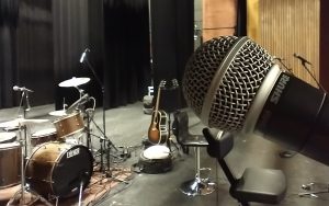 Gros plan d'un microphone sur une scène, avec divers instruments de musique en arrière-plan.