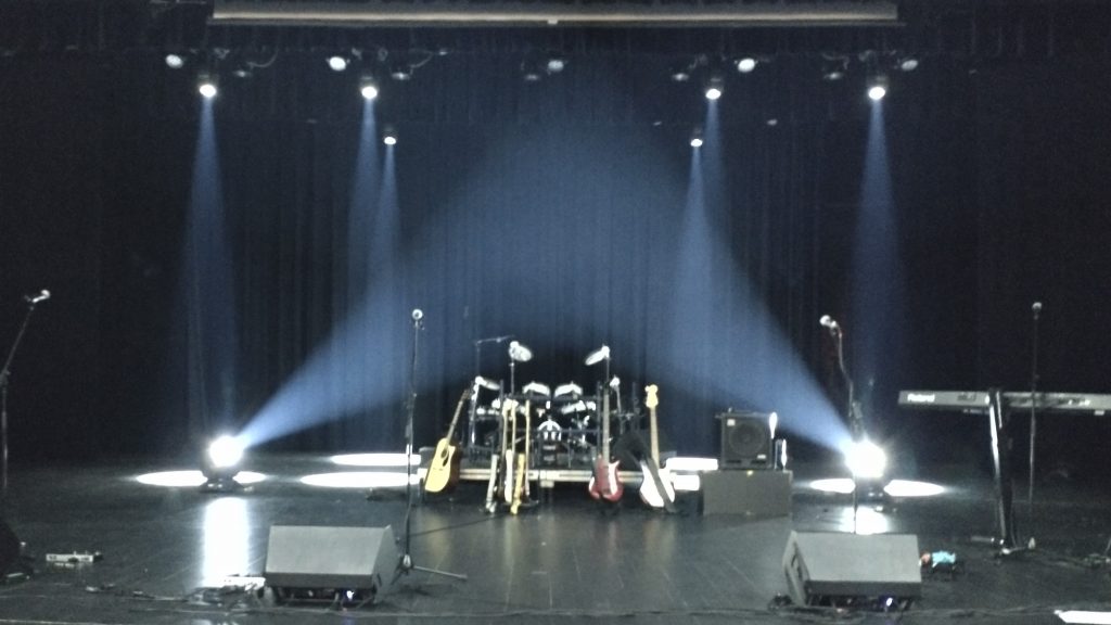 Vue d'ensemble de la scène du théâtre Gilles-Laplante, munie d'instruments éclairés par des faisceaux blancs.