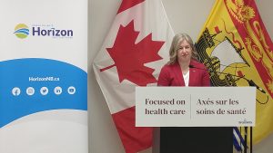 Photographie de la première ministre du Nouveau-Brunswick Susan Holt derrière un lutrin et le slogan bilingue "Axés sur les soins de santé".