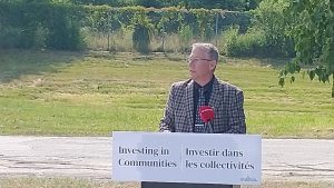 Photographie du ministre Lepage en plein discours, avec un terrain vague en arrièere-plan.