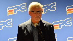 Photographie de Kevin Russell en pleine allocution, avec les couleurs du Parti progressiste-conservateur du Nouveau-Brunswick en arrière-plan.