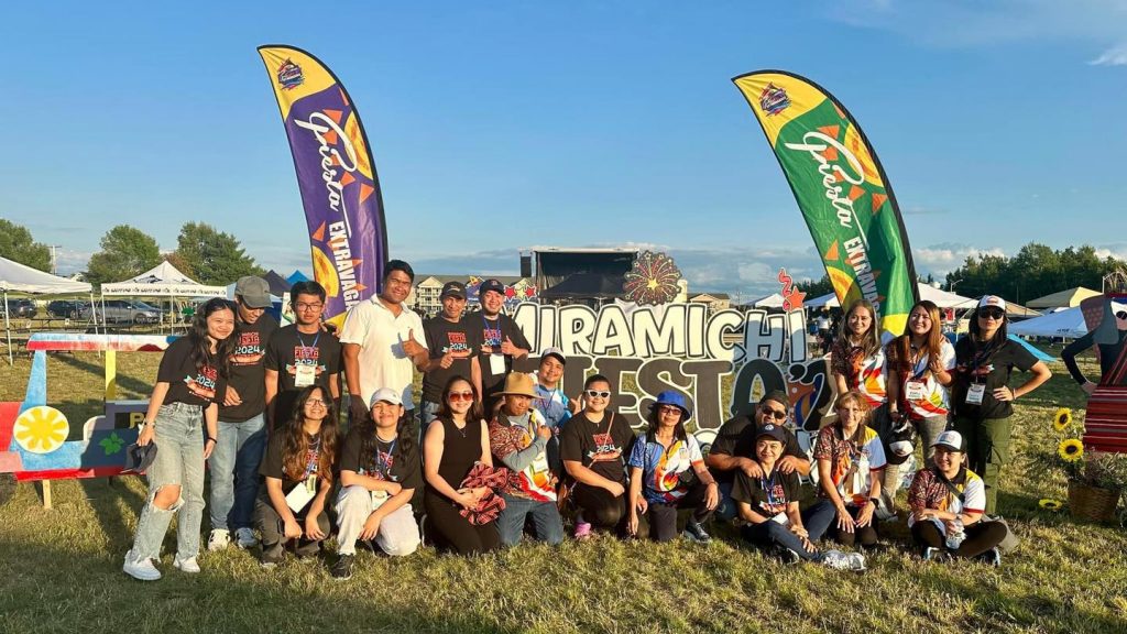 Photographie de groupe devant des bannières aux couleurs de la Fiesta Extravaganza de Miramichi.