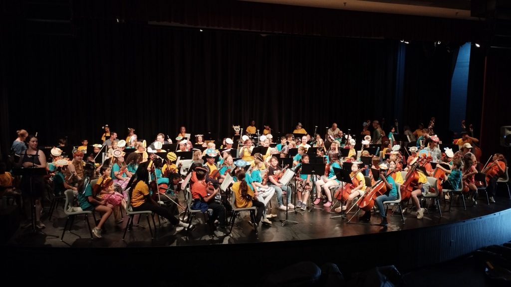 125 enfant sur scene habillés de t-shirt colorés et avec chacun leur instrument