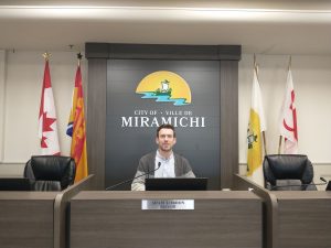 Photographie du maire de Miramichi Adam Lordon, assis à sa place dans la salle du conseil municipal.