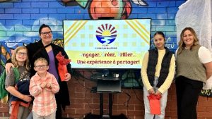 Photographie de la directrice Annie Breau accompagnée d'une mère et trois élèves, autour du nouveau logo de l'École Carrefour Beausoleil.