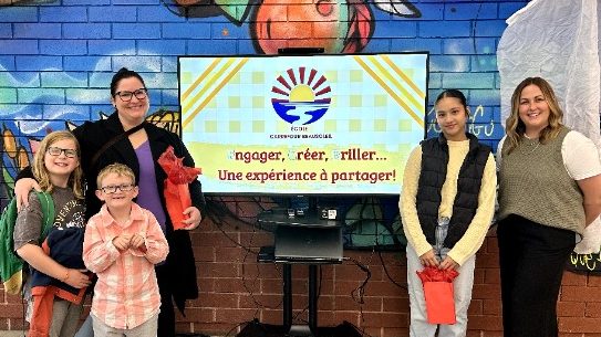 Photographie de la directrice Annie Breau accompagnée d'une mère et trois élèves, autour du nouveau logo de l'École Carrefour Beausoleil.