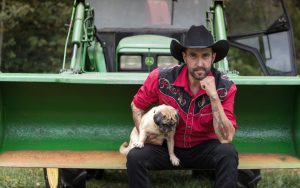 Photographie de John Boulay, assis dans une pelle de tracteur mécanique, tenant un chien.