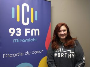 La conseillère municipale Véronique Arsenault pose aux côtés du logo de C93 Miramichi.