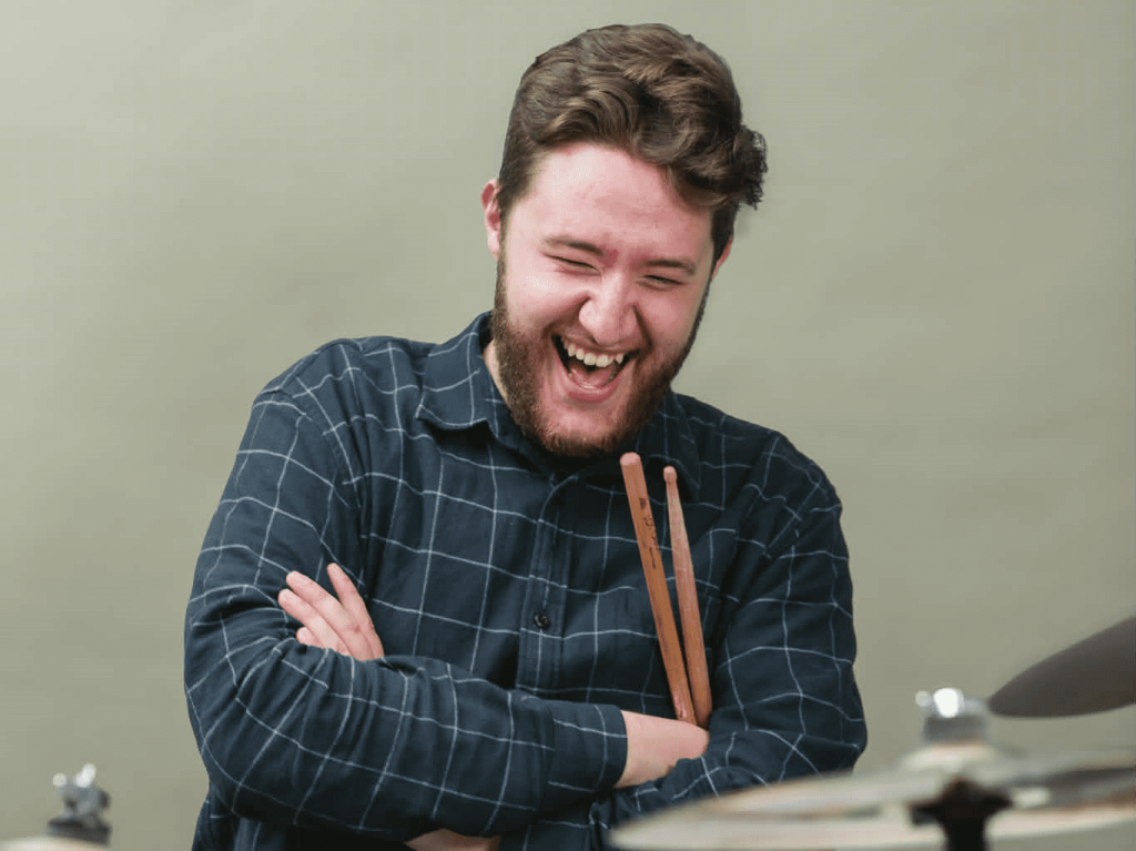 Photographie de Luc Poirier, souriant, avec des cymbales à l'avant-plan.