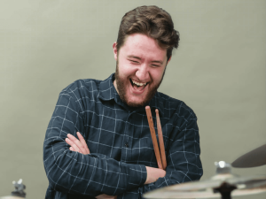 Photographie de Luc Poirier, souriant, avec des cymbales à l'avant-plan.