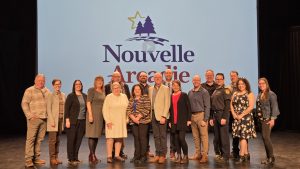 Photographie de groupe incluant les membres du conseil municipal de Nouvelle-Arcadie devant le logo tout juste dévoilé de Nouvelle-Arcadie.