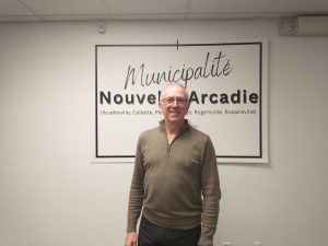 Photographie du maire Jimmy Bourque devant une affiche de la municipalité de Nouvelle-Arcadie.