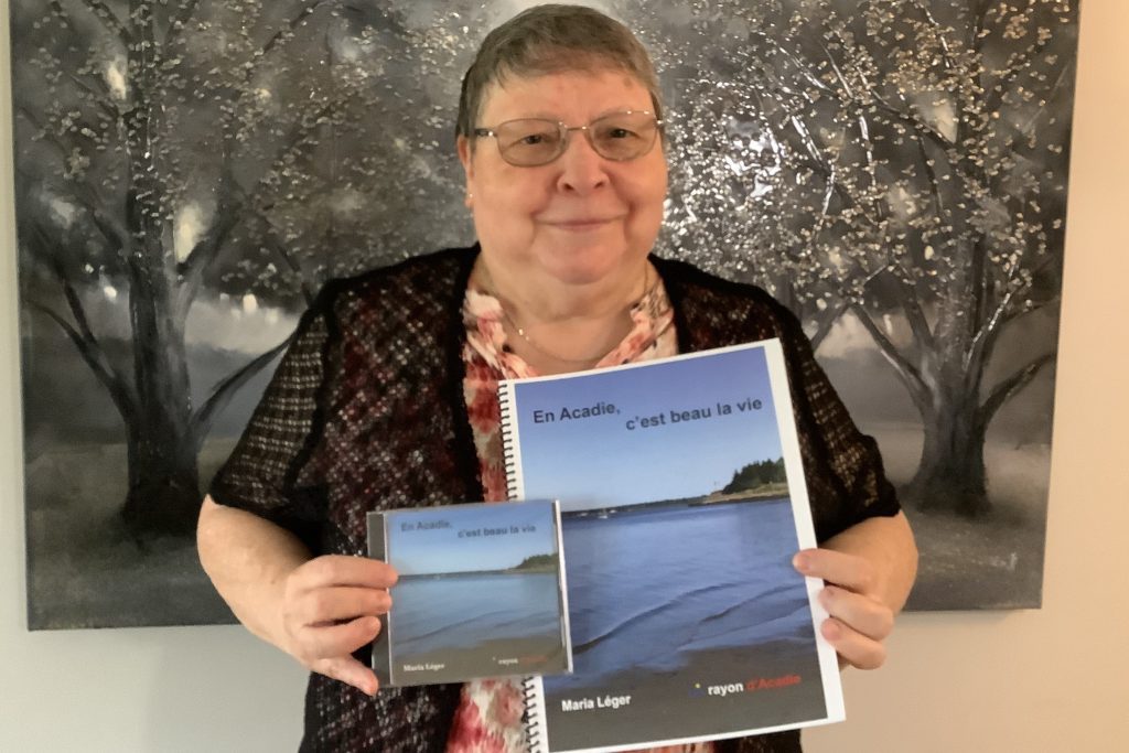 Photographie de Maria Léger tenant un exemplaire de son album et de son livret de chansons.