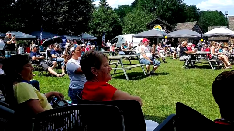 Photographie montrant un public nombreux assis à l'extérieur.