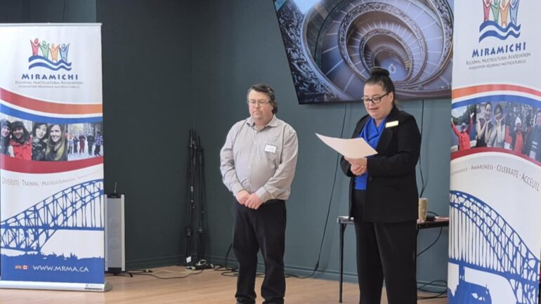 Photographie de Craig Silliker et Juliette Cabana aux côtés de bannières aux couleurs de l'Association régionale multiculturelle de Miramichi.